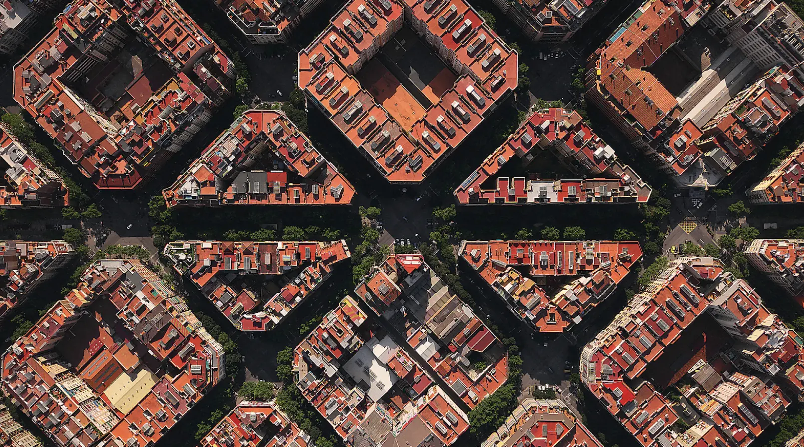 Aerial view of a dense urban neighborhood with red-roofed buildings arranged in repeating geometric blocks separated by streets and green courtyards.