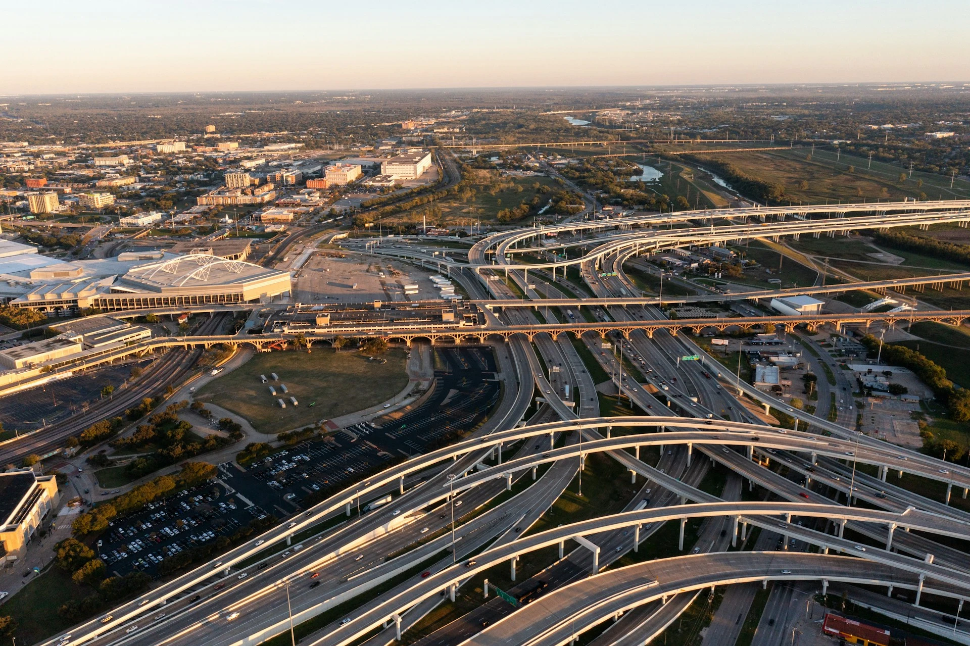Aerial view of a large highway interchange with multiple elevated roads curving and intersecting over an urban landscape at sunset.